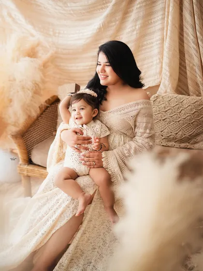 A beautiful mother holding her daughter, both looking radiant in their matching boho-style outfits.
