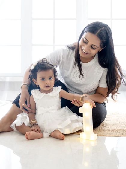 A mother and daughter moment during a first birthday shoot, playing with a light-up number "1" prop.