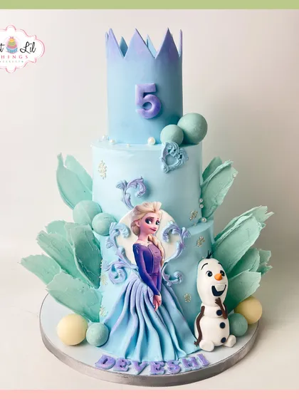 A grand Frozen-themed cake for a 5th birthday. This multi-tiered creation features Elsa, Olaf, and a magnificent ice-blue crown, decorated with sugar icicles and snowflakes.