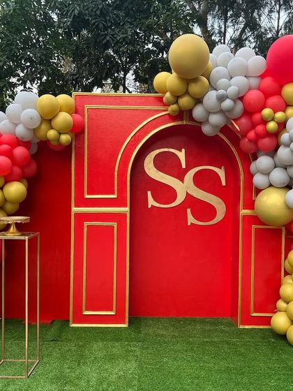 A vibrant red and gold 50th birthday celebration. This outdoor setup includes a custom monogrammed backdrop and a playful balloon arch, perfect for a daytime party.