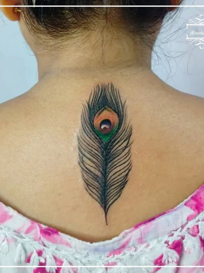 A vibrant, colored peacock feather tattooed down the spine. The rich greens, blues, and orange of the feather's "eye" are carefully blended to create a realistic and beautiful effect.