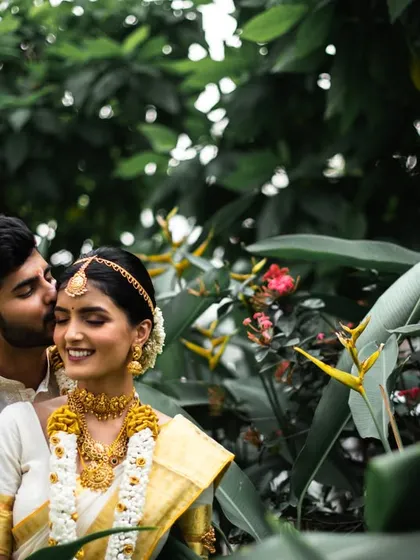 A sweet and romantic moment, with the groom kissing the bride's cheek. The natural, leafy background adds to the charm.