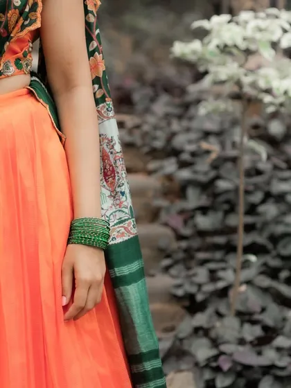 The pleated orange Mangalagiri silk skirt paired with the bottle green Kalamkari-style dupatta creates a stunning contrast in this half saree ensemble.