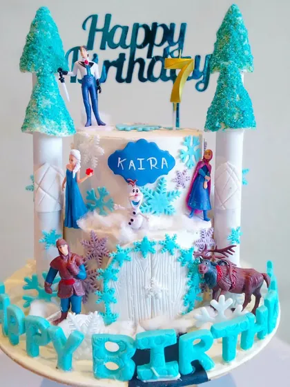 A magical Frozen-themed castle cake for a 7th birthday. This two-tiered cake is decorated with edible snowflakes, ice castles, and figurines of Elsa, Anna, Olaf, and other characters.