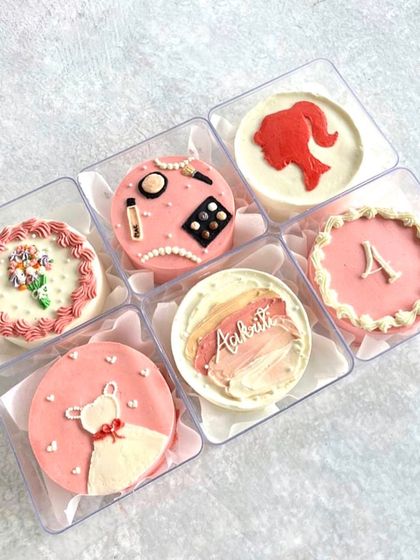 A set of six pretty-in-pink mini bento cakes for a 4th birthday, with themes like Barbie, makeup, and flowers.
