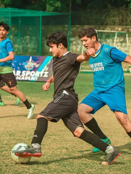 A player in a black jersey is challenged by a defender in a blue bib.