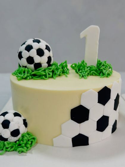 Goal! This football-themed cake was a huge hit for a first birthday party. It features edible soccer balls, piped grass, and a fun hexagonal pattern.