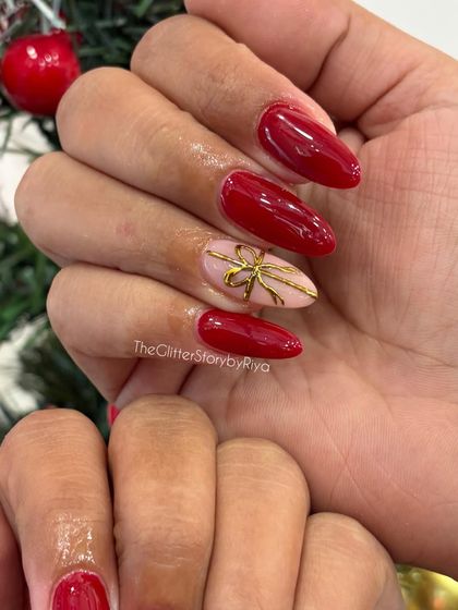 A classic Christmas look with glossy red nails and a single accent nail featuring a delicate, hand-painted gold bow.