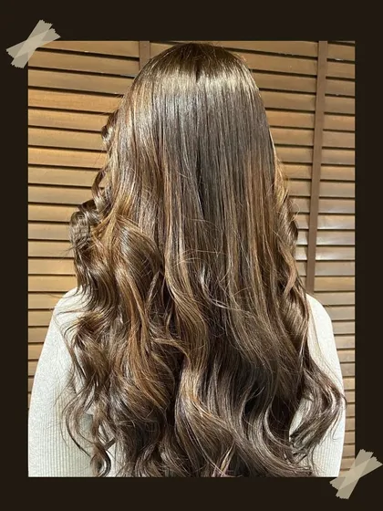 A close-up of long, healthy hair with a rich brown balayage. The soft curls at the ends add volume and showcase the multi-dimensional color.