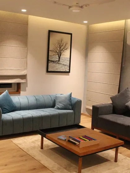 In this family lounge, we combined different seating options, including a vibrant blue sofa and a neutral gray one, to create a relaxed and versatile space. Roman blinds offer soft light diffusion, while the light wood flooring adds warmth underfoot.