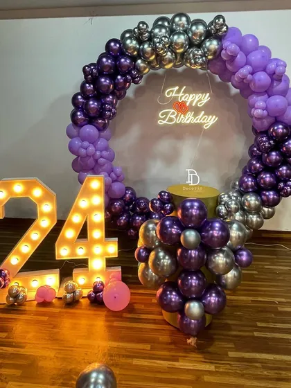 A 24th birthday celebration with a striking purple and silver color scheme. This setup includes a full ring balloon arch, a 'Happy Birthday' neon sign, and large '24' marquee numbers.