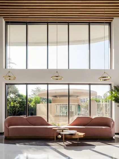 A waiting area with elegant, curved sofas and double-height windows that look out onto a green space. The design uses natural light and sophisticated forms to create a calm and beautiful environment.