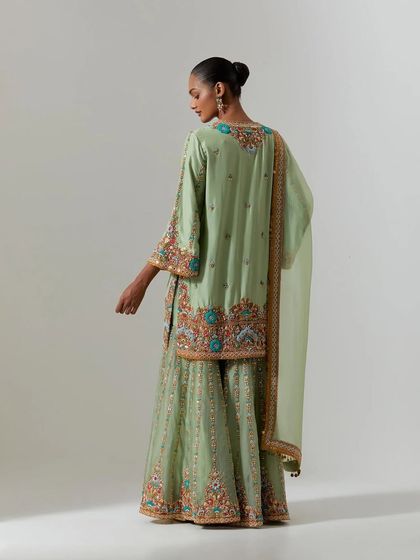 The back view of a pista green sharara set, showing the intricate, colorful embroidery that adorns the hem of the kurta and the flowy pants.