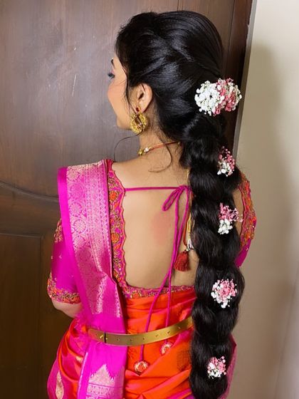 A beautiful long braid decorated with fresh pink and white flowers, perfectly matching the bride's vibrant saree for her special day.