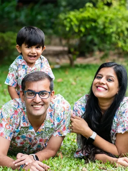 A relaxed family portrait with parents and their son lying on the grass, all wearing matching floral shirts.