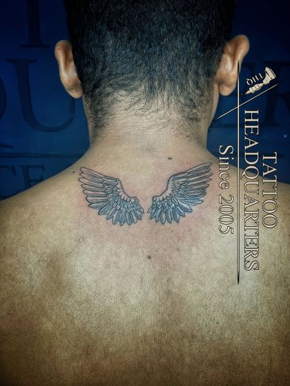 A pair of angel wings tattooed on the upper back, a classic symbol of freedom, protection, and spirituality.