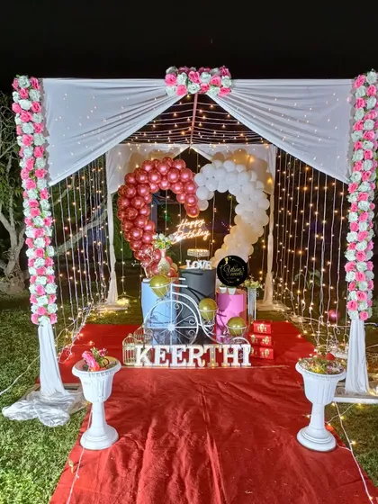 A romantic outdoor canopy setup, perfect for a surprise proposal or an intimate birthday celebration. The design features flowing white drapes, fairy lights, and a heart-shaped balloon arrangement.