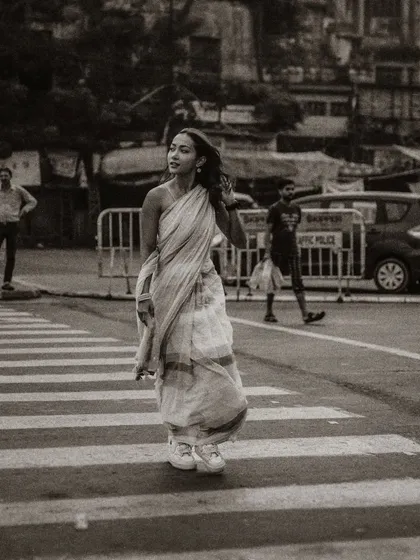 A black and white street photograph of a model crossing the road. The grainy texture and candid moment give this shot a classic, photojournalistic feel.