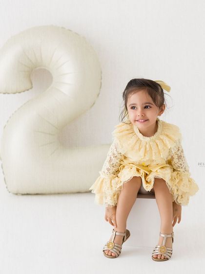 A sweet, seated portrait of a little girl on her second birthday. Her lacy yellow dress and the simple background create a timeless look.