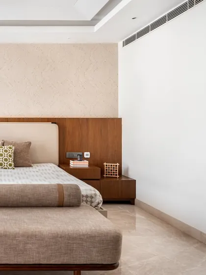The master bedroom at Noor Haus is a sanctuary of calm. The bed-back wall extends across the room, featuring a textured, rope-like wallpaper over warm wood panels for a soft, layered effect.