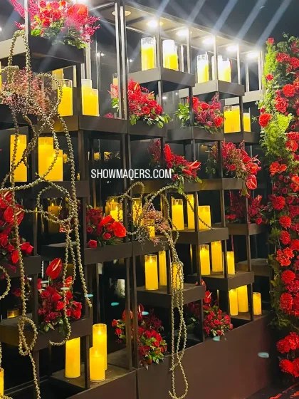 A close up of the candle wall installation, showcasing the interplay of warm candlelight and vibrant red floral arrangements.