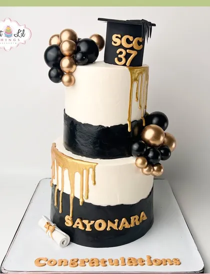 A stylish black, white, and gold two-tiered cake celebrating a graduation. The gold drip and graduation cap add a touch of class.