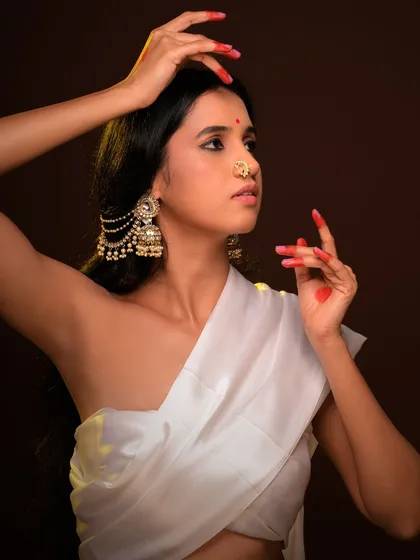 This pose, with the model's hands framing her face, showcases the traditional makeup and jewelry in a style reminiscent of classical Indian paintings.
