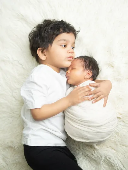 A tender moment between brothers. The older sibling carefully holds his newborn brother, showcasing a bond that will last a lifetime.