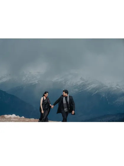 A wide shot of a couple walking hand-in-hand on a mountain ridge, showcasing the vastness of the landscape and their journey together.