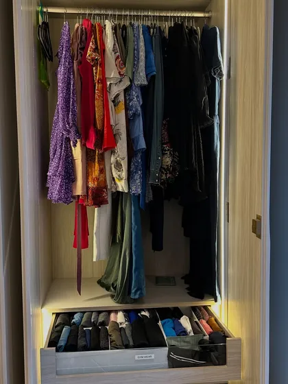A drawer filled with neatly folded clothes sits below a rail of hanging dresses and tops.