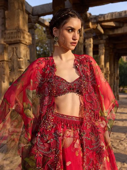 A bold red floral print cape and bustier set, featuring intricate embellishments for a glamorous, high-fashion look.