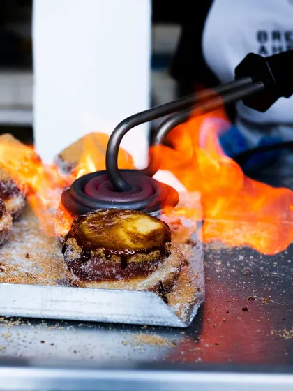 A close-up action shot of the branding iron hitting the donut at Bread Ahead Bakery, capturing the heat and caramelization in detail.