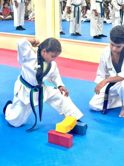 A young girl shows her power and focus by breaking boards during her belt test, a key part of demonstrating proficiency.