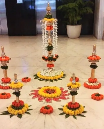 An intricate and traditional floral arrangement for a lobby or entrance. This display features decorated lamps (diyas) and a central floral tower made from marigolds and jasmine, all arranged in a beautiful rangoli pattern.