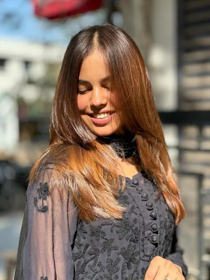 A beautiful shot of a client enjoying her new hair. The color is a warm, multi-tonal brown that looks natural and sophisticated, enhanced by a sleek, layered cut.