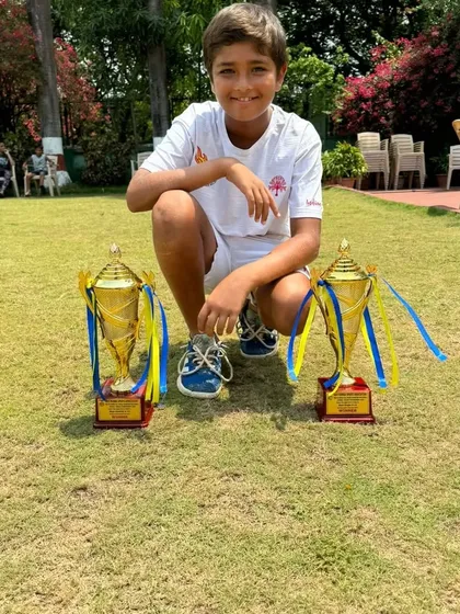 Aarav crouching with his two trophies on the grass, a creative shot celebrating his double win.