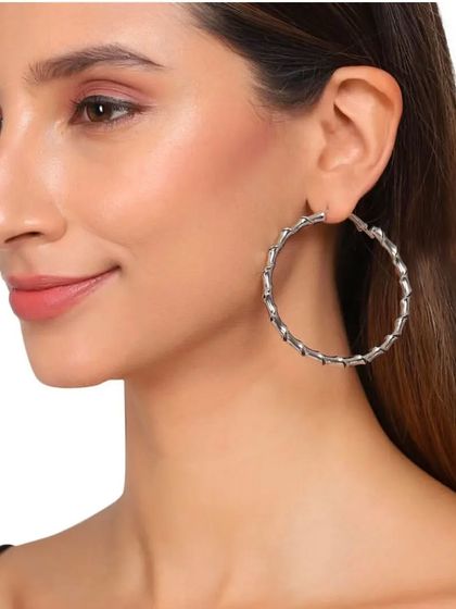 A model wearing the twisted metal hoop statement earrings, showing their size and how they look with a simple top.