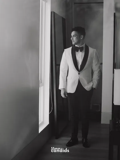 A black and white portrait of the groom, Rohan, looking sharp in his tuxedo. The moody lighting adds a touch of classic elegance.