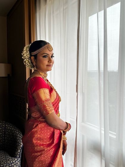 A serene portrait by the window. The natural light highlights her glowing skin and the rich gold of her saree and jewelry.