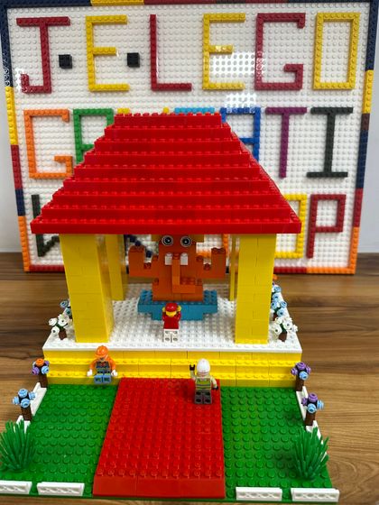 A detailed LEGO pandal with a small Ganesha idol inside, built during our workshop. The background features a "J.E. LEGO GANPATI WORKSHOP" sign made of bricks.