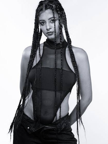 A standing pose from the same series, where the model's braids and sheer bodysuit create interesting lines and textures against the clean white background.