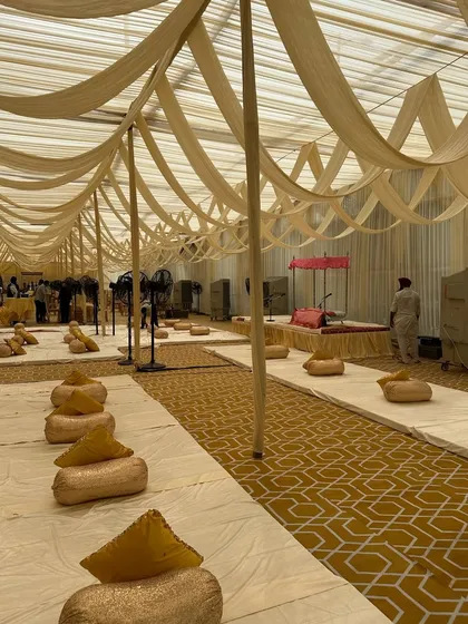 An inside view of the spacious tent decorated for a religious event. We arranged neat rows of floor seating with cushions, ensuring a comfortable and organized space for the devotees.