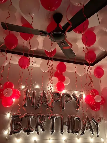 Kamre ki ceiling par red aur white balloons aur 'Happy Birthday' ke silver foil letters se ki gayi yeh decoration bahut sundar lagti hai. Saath mein fairy lights bhi hain.