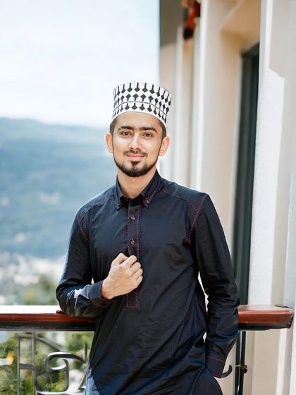 A young client wears a classic black Pathani suit with subtle red stitch detailing. Paired with a traditional prayer cap, this look is perfect for religious ceremonies and festive occasions.