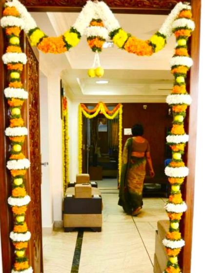 A traditional main door flower decoration for a housewarming. The entrance is adorned with garlands of marigold and jasmine flowers.