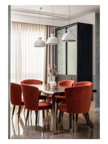 The dining area features deep orange corduroy chairs that add a pop of color and texture. They complement the live-edge walnut table and the custom Pichwai painting of Lord Balaji, which was created to match the home's color palette.