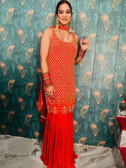 A full-length photo of a happy client in a red sharara suit, perfect for a wedding party.