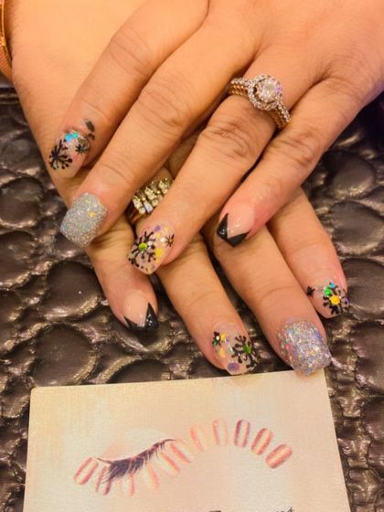 A unique and artistic set for a special occasion. The design features a mix of black tips, silver glitter nails, and accent nails with colorful, abstract snowflake patterns.