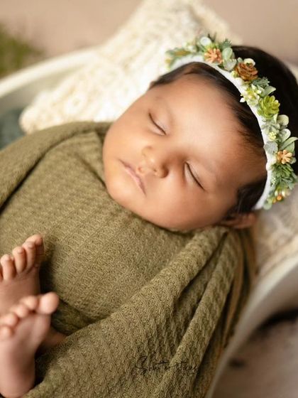 A newborn wrapped in an olive green waffle wrap with a succulent headband, showcasing a beautiful, earthy theme.