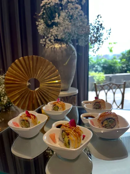 Freshly rolled sushi elegantly arranged on a mirrored table, reflecting the beautiful floral decor of the anniversary party.